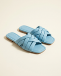Light-blue woven-strap flat slide sandals on a warm ivory studio background